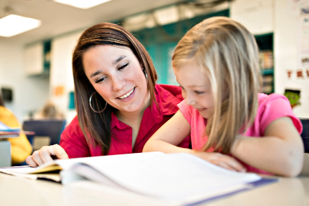 A young girl and her teacher reading a book at her desk