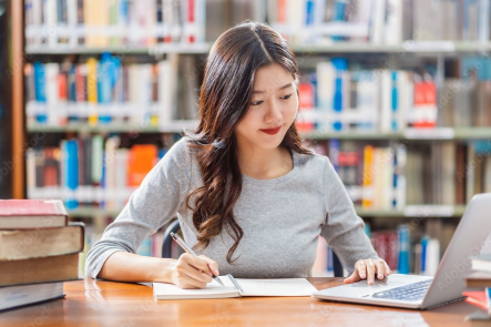 A female college student taking notes with a laptop in a library