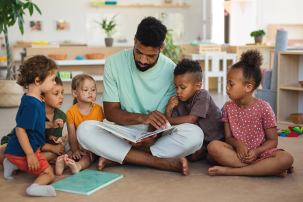A group of preschool students gathered around a teacher reading a book